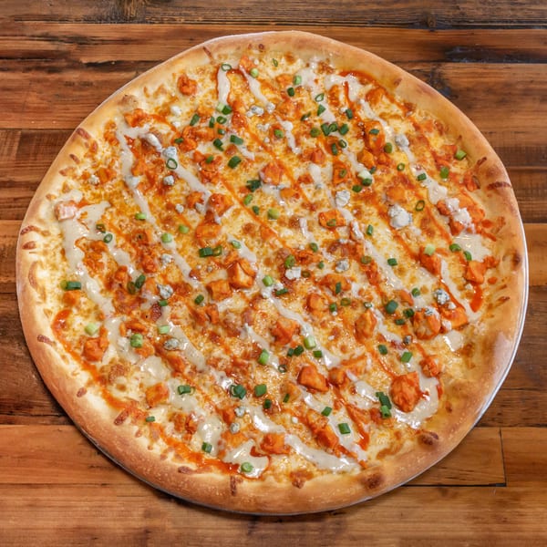 NY Pie's buffalo chicken pizza with ranch, blue cheese crumbles, and green onions on a wooden table.